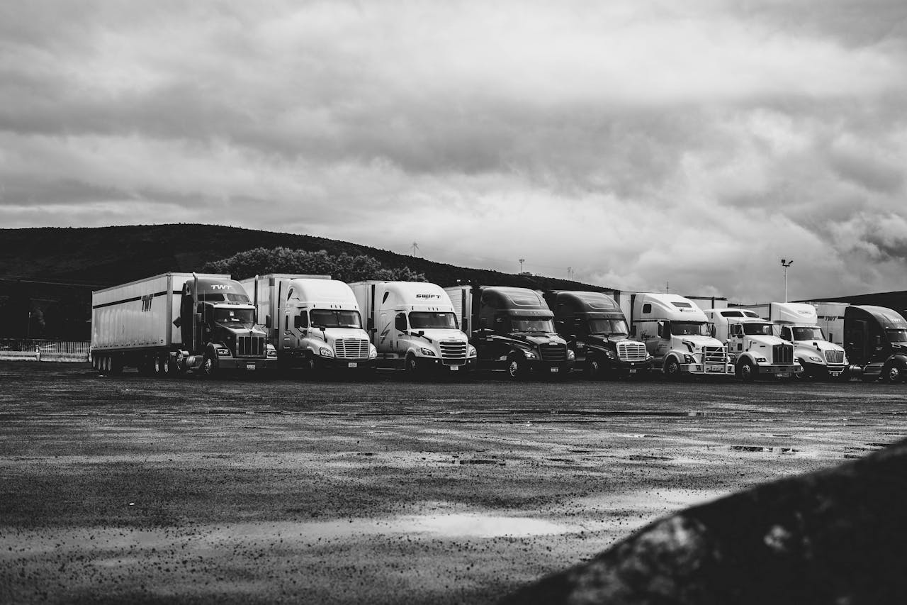 Services Row of parked semi trucks in a rainy lot, captured in a dramatic black and white setting.