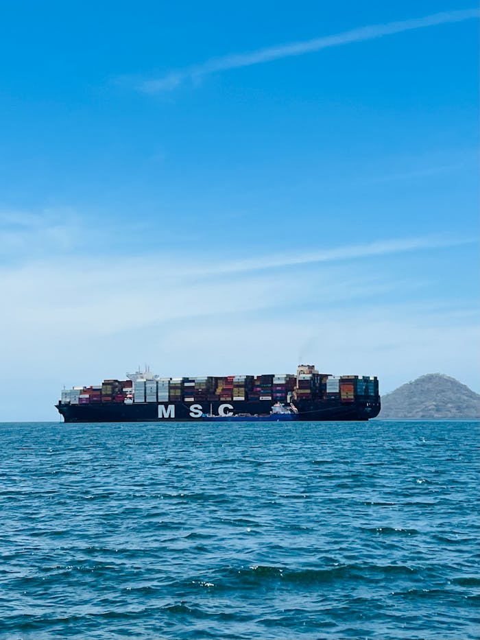 Services Large cargo ship carrying containers on a calm ocean with a clear blue sky.