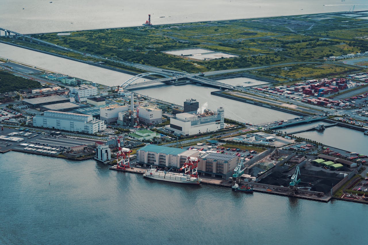 Home Aerial view of Tokyo's industrial port by the water, featuring cranes and containers.